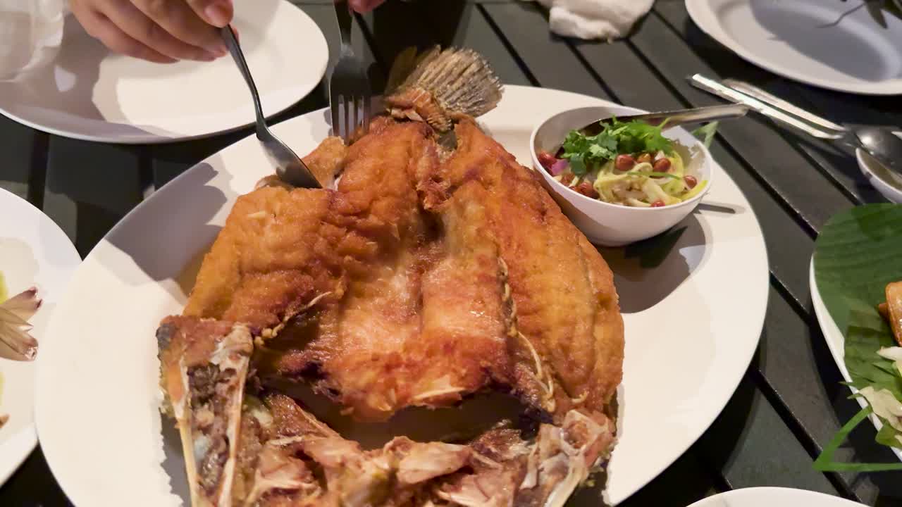 Hand portions crispy sea bass at outdoor dining table, natural daylight, overhead camera angle