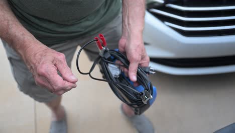 senor citizen hands carefully wind up a jump starter battery charger after use