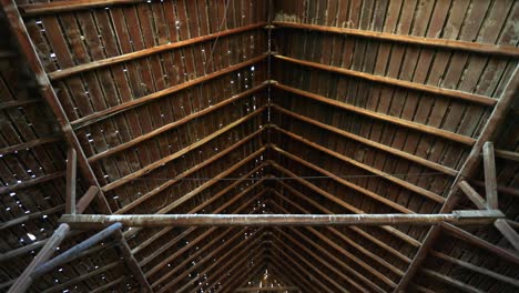 a downward panning shot showing a large open barn with exposed wooden beams, revealing straw bales under tarps