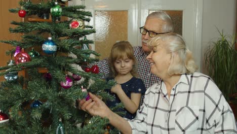 Children-girl-with-grandparents-couple-decorating-artificial-Christmas-pine-tree-at-old-fashion-home