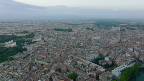 Town-buildings-in-historic-city-centre-from-height.-Backwards-reveal-of-tourist-landmarks-and-bend-of-Tiber-river.-Rome,-Italy