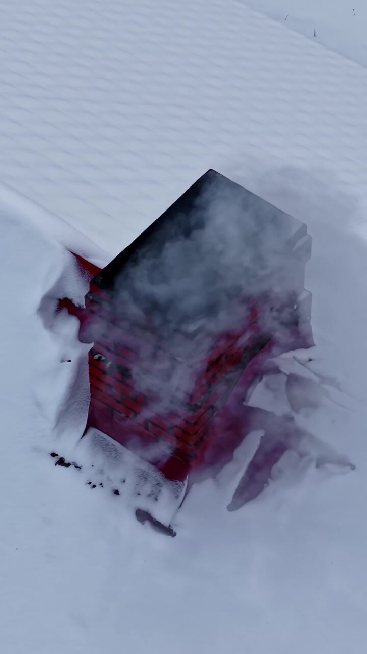 Un camino in mattoni rossi emette fumo su un tetto coperto di neve. La scena suggerisce un interno caldo in un ambiente freddo. Adatto per temi invernali o studi architettonici.