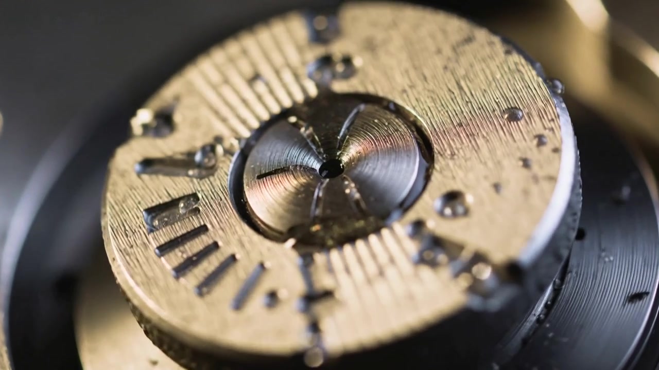 Shifting camera focus showing turning metal component in fixture with oil droplets for inspection
