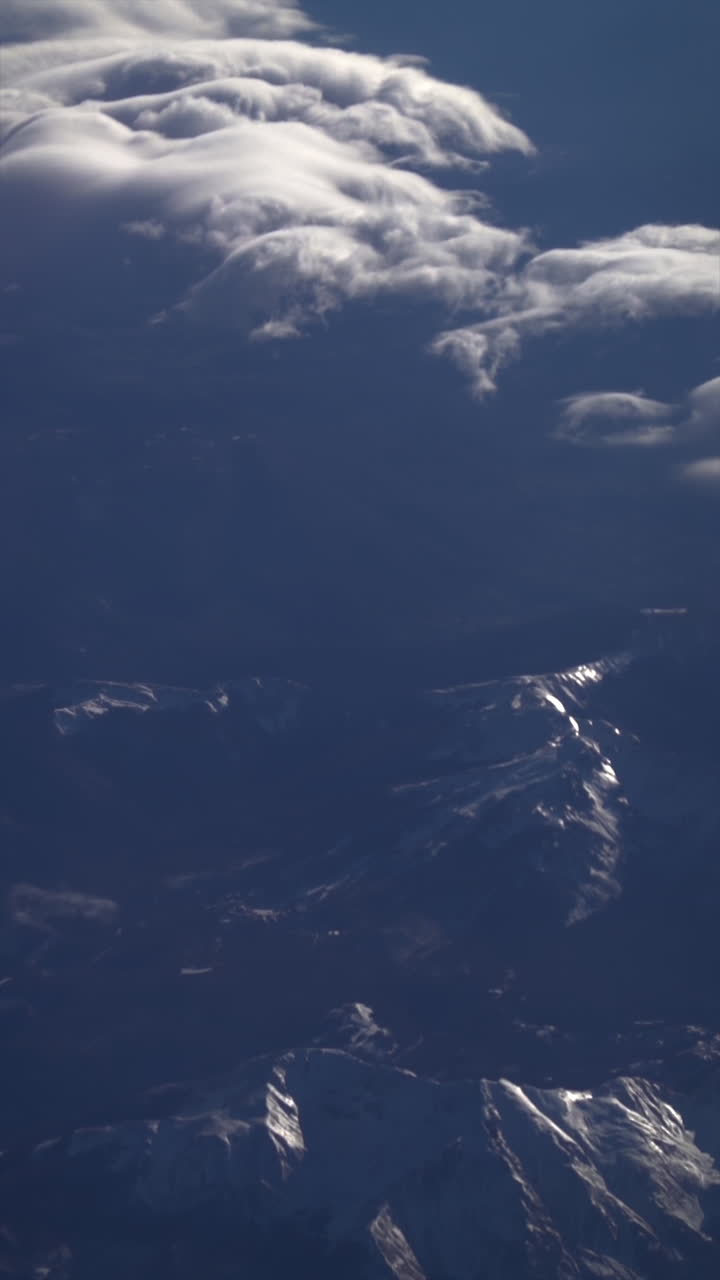 View from an airplane window of clouds over a mountain range. Vertical