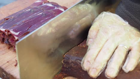 a butcher cuts a piece of pastirma with a large knife.