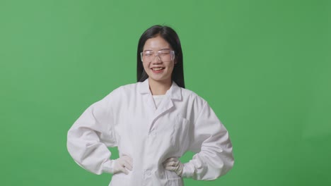 asian woman scientist with arms akimbo looking at camera and smiling while standing on the green screen background in the laboratory