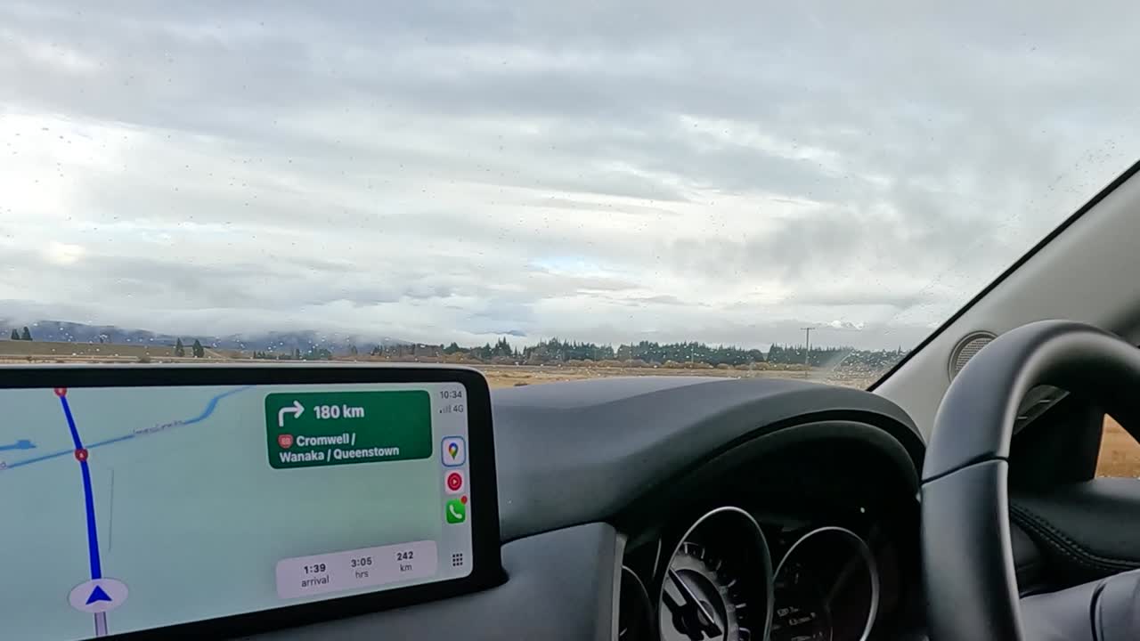 Uno schermo di navigazione digitale mostra le indicazioni del percorso mentre si guida attraverso un paesaggio rurale panoramico.