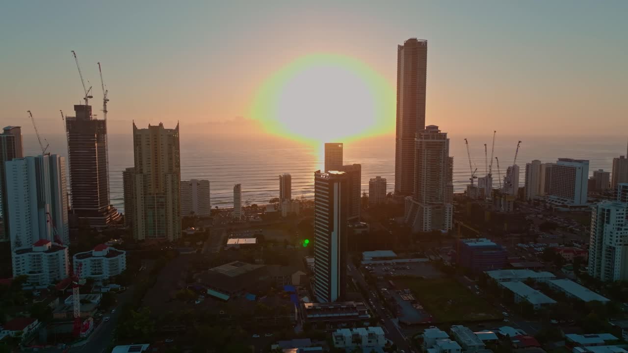 Aerial view showcases the Gold Coast skyline at sunrise, with warm golden light reflecting off skyscrapers captured from the peaceful vantage of Budds Beach