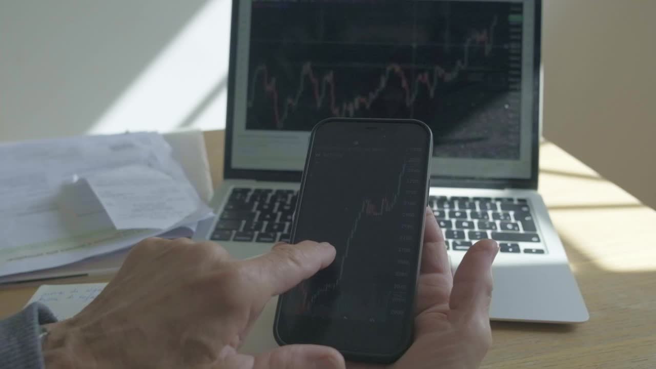 anciana anciana jubilada que sostiene un teléfono inteligente y una computadora portátil con análisis de inversión en el mercado de valores y comercio en línea en cámara lenta