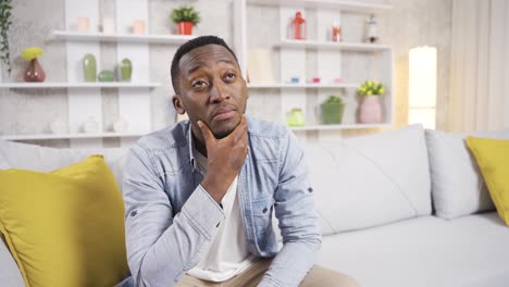 Nervous-and-worried-african-man-sitting-alone-at-home-on-sofa-and-drinking-coffee.