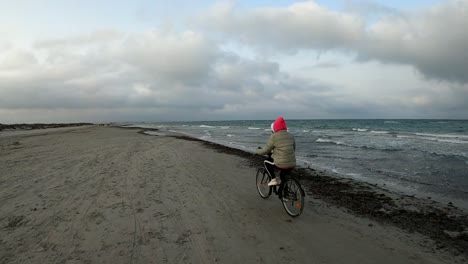 biker woman riding bike through the beach at sunset in slow motion