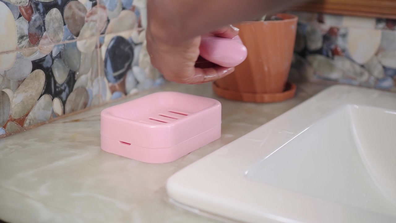 Hand Picking Up Pink Bar of Soap from Dish in Bathroom