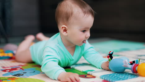 playful kid lying on belly and waving his toy. beautiful baby showing tongue. close up. blurred backdrop.