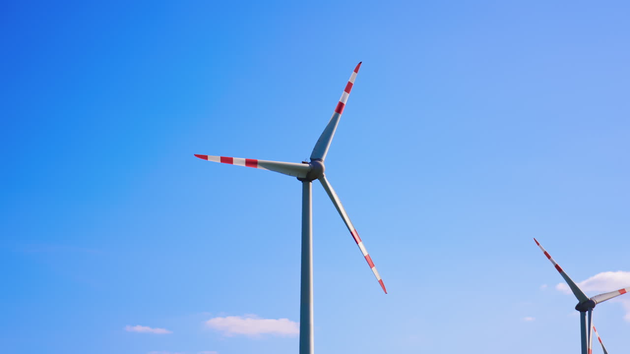 Wind turbines produce clean energy. Tall wind turbines with red and white blades spin against a clear blue sky, showcasing renewable energy in action