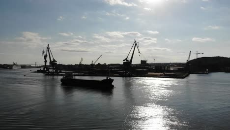 Cargo-ship-passing-river-in-Gothenburg-industrial-port,-Aerial-view-on-sunny-day,-Sweden