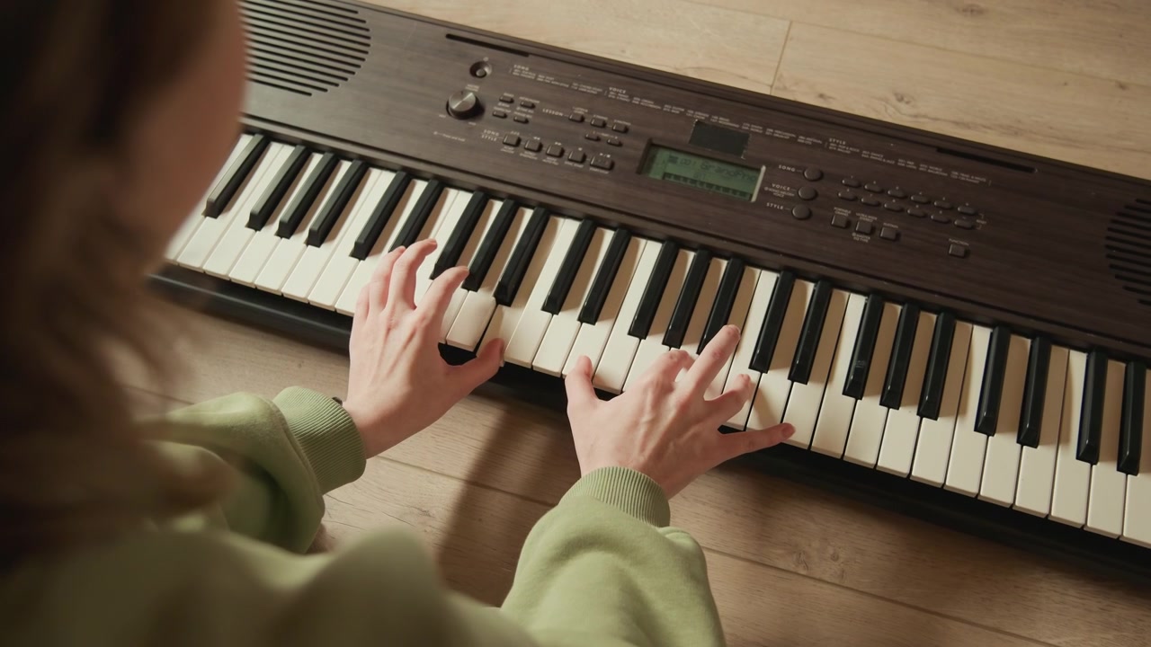 Lähikuva henkilöstä soittamassa vintage-elektronista kosketinsoitinta molemmilla käsillä painaen koskettimia, muodostaen sointuja ja liikkuen säestyksen läpi lämpimässä sisävalossa hienovaraisella liikesumennuksella ja tarkasti.