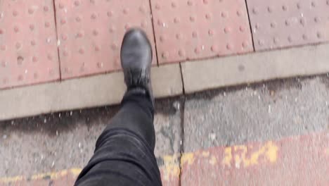 POV-man's-legs-walking-through-urban-city-streets,-stylish-boots-and-dark-jeans