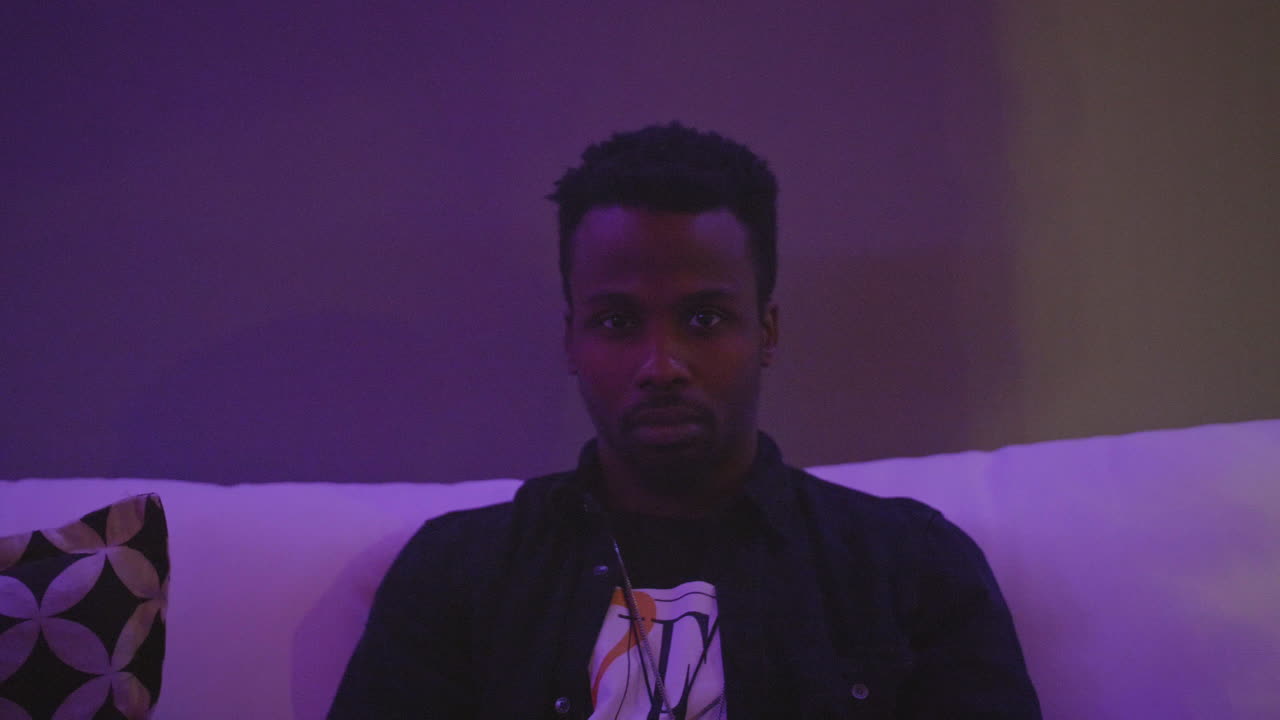 Uomo afroamericano assorto nei pensieri mentre ascolta una discussione, con luci che cambiano colore.