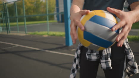 close up of man with plaid shirt around waist bouncing volleyball in outdoor sports arena with sports equipment in background, capturing action in recreational environment