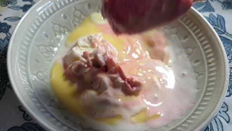 Strawberry,-vanilla-and-black-current-flavored-ice-cream-with-yellow-vanilla-custard-topping,-delicious-sunday-dessert-being-scooped-with-stainless-steel-spoon-in-porcelain-bowl