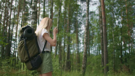 A-young-woman-with-a-mobile-phone-walks-through-the-forest-traveling-with-a-backpack-in-slow-motion.-Traveler-in-shorts-in-the-woods-looking-for-gps-satellites