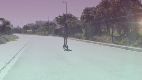 Spots-of-light-against-rear-view-of-african-american-woman-riding-electric-scooter-on-the-street