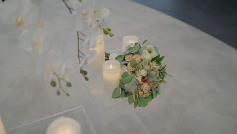 Elegant-wedding-bouquet-placed-on-a-glass-table-with-lit-candles-and-orchids