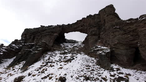 immersive fpv journey skimming the waters of lake caviahue past snow-dusted basalt columns and soaring through a rugged volcanic famous stone bridge in the andes, captured in dynamic aerial motion