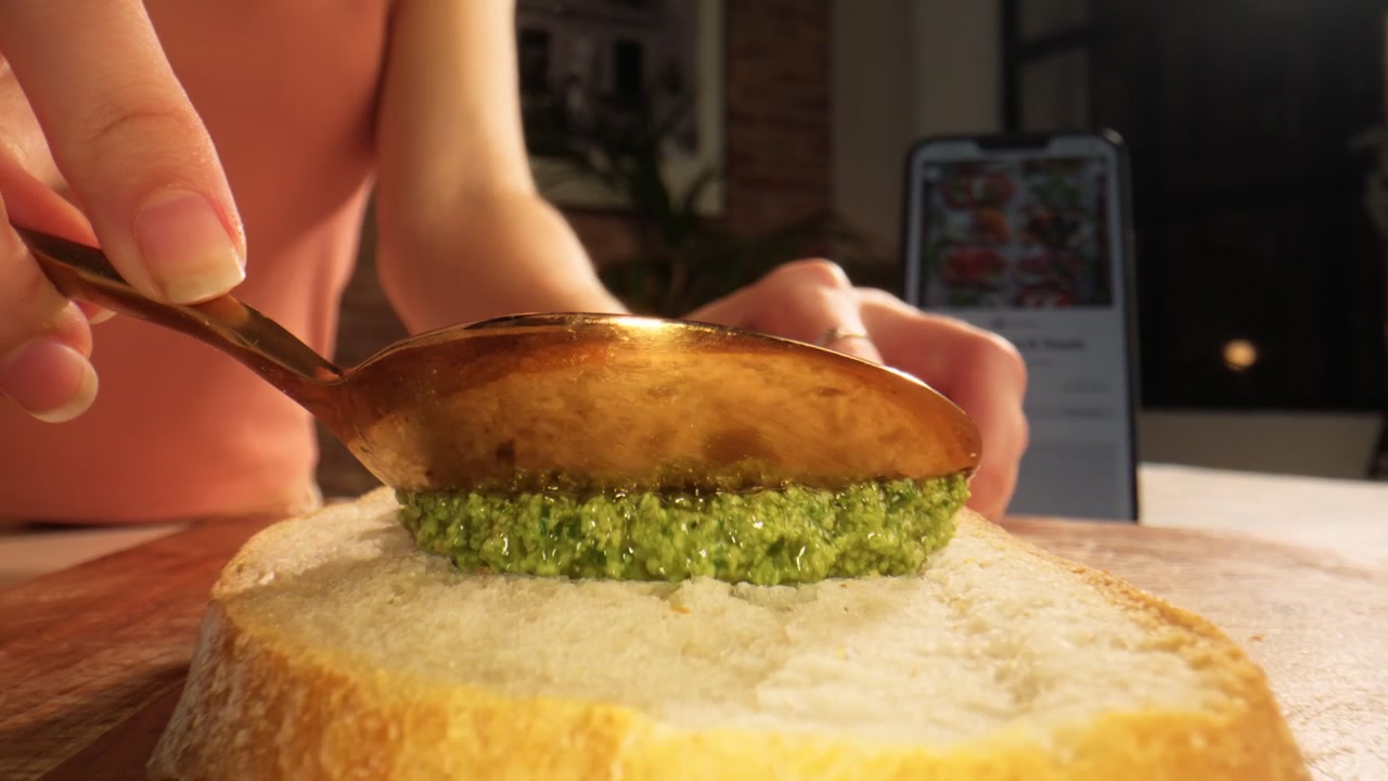 Primeros planos macro muestran una cuchara untando pesto verde fresco sobre pan rebanado
