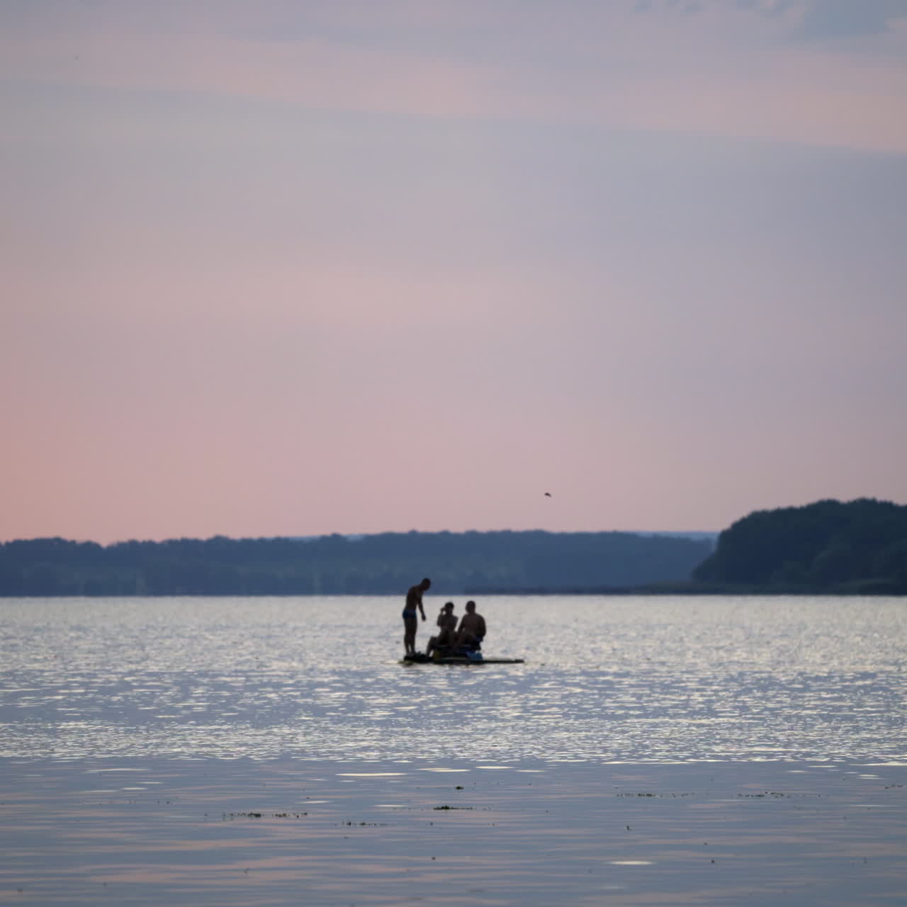 Young men floating in a catamaran on the river. Water background and two guys sitting in pedal boat while one man standing near in the evening.