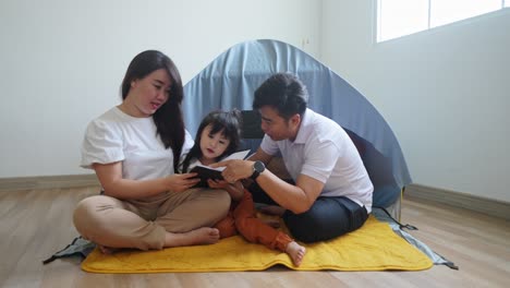 asian parents teaching little girl daughter doing homework while sitting in front of tent at home