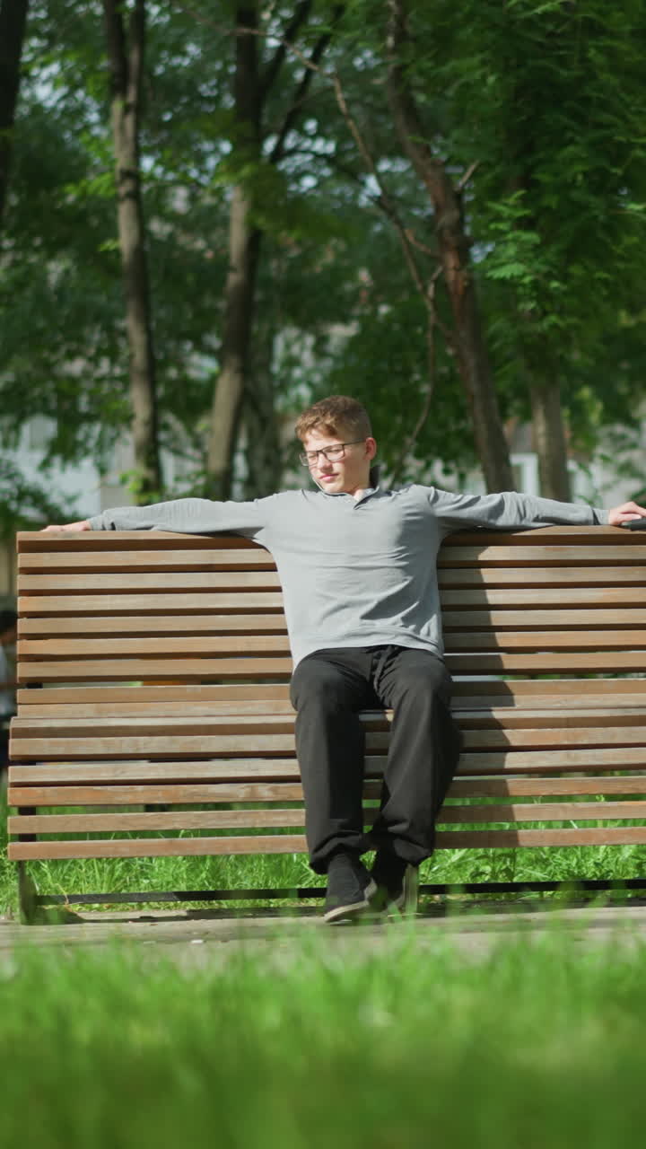 어린 소년은 공원 벤치에 어, 그리고는 그의 자전거로 돌아보고, 근처에, 누군가는 다른 벤치에서 앉아, 그리고 다른 사람들은 뒷면에 초록색과 함께 나무로 둘러싸인 공원을 산책