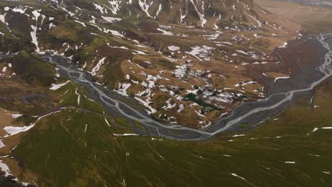 Luftaufnahme-über-Einen-Fluss,-Der-Durch-Mit-Schmelzendem-Schnee-Bedeckte-Berge-Fließt,-An-Einem-Bewölkten-Und-Nebligen-Tag-In-Island