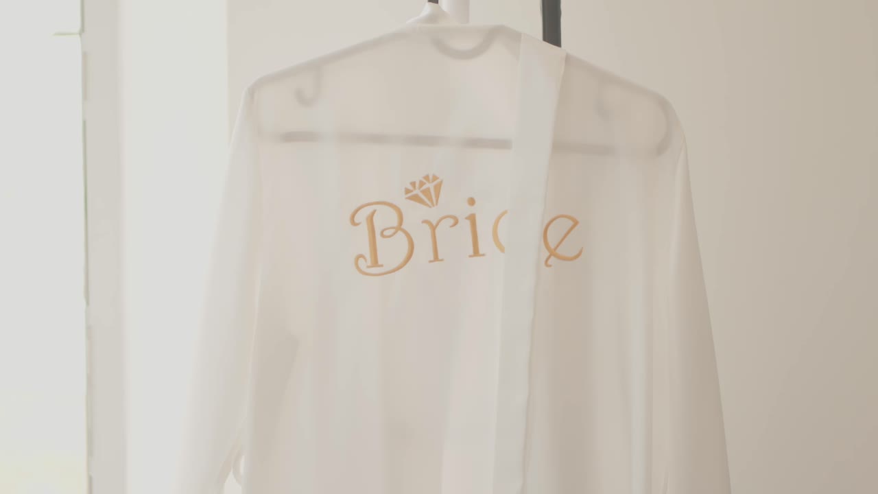 White bridal robe with gold "Bride" text and diamond graphic on hanger near soft light
