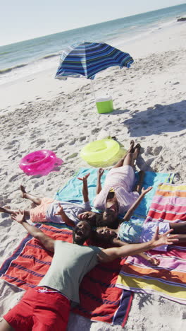 vertical video of happy african american family having fun on beach, lying on sand