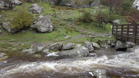 Idyllische-Holzbrücke-über-Dem-Wasserfall-Im-Tal,-Der-Rechts-In-Eine-Kraftvoll-Fließende-Flusspfanne-Stürzt