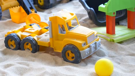 closeup of a yellow toy truck in a sandbox with other toys.