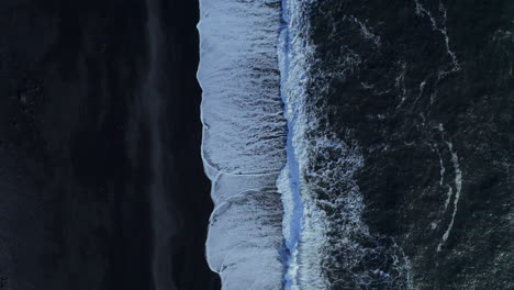 white surf waves rolling on black sand -top view