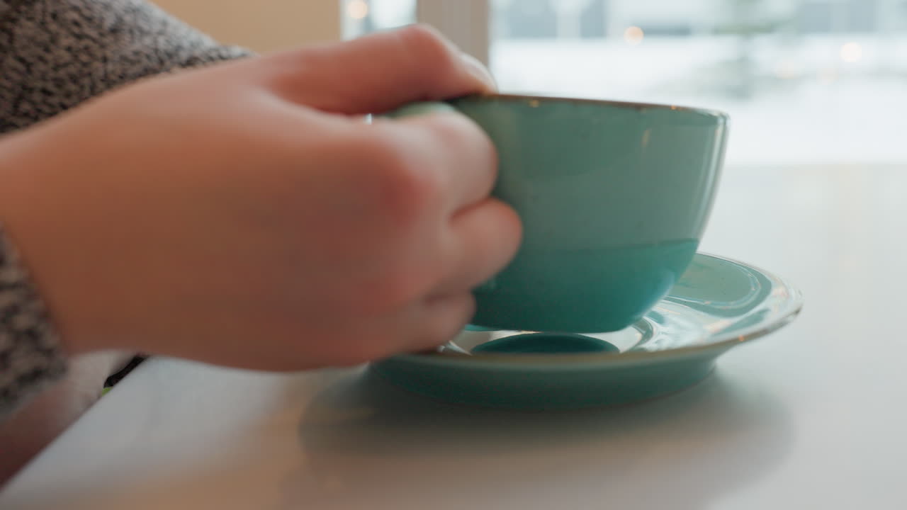 Charming young woman enjoying cold drink in cozy cafe with winter street view outside, decorated with Christmas lights, seen through the window, creating a peaceful holiday atmosphere