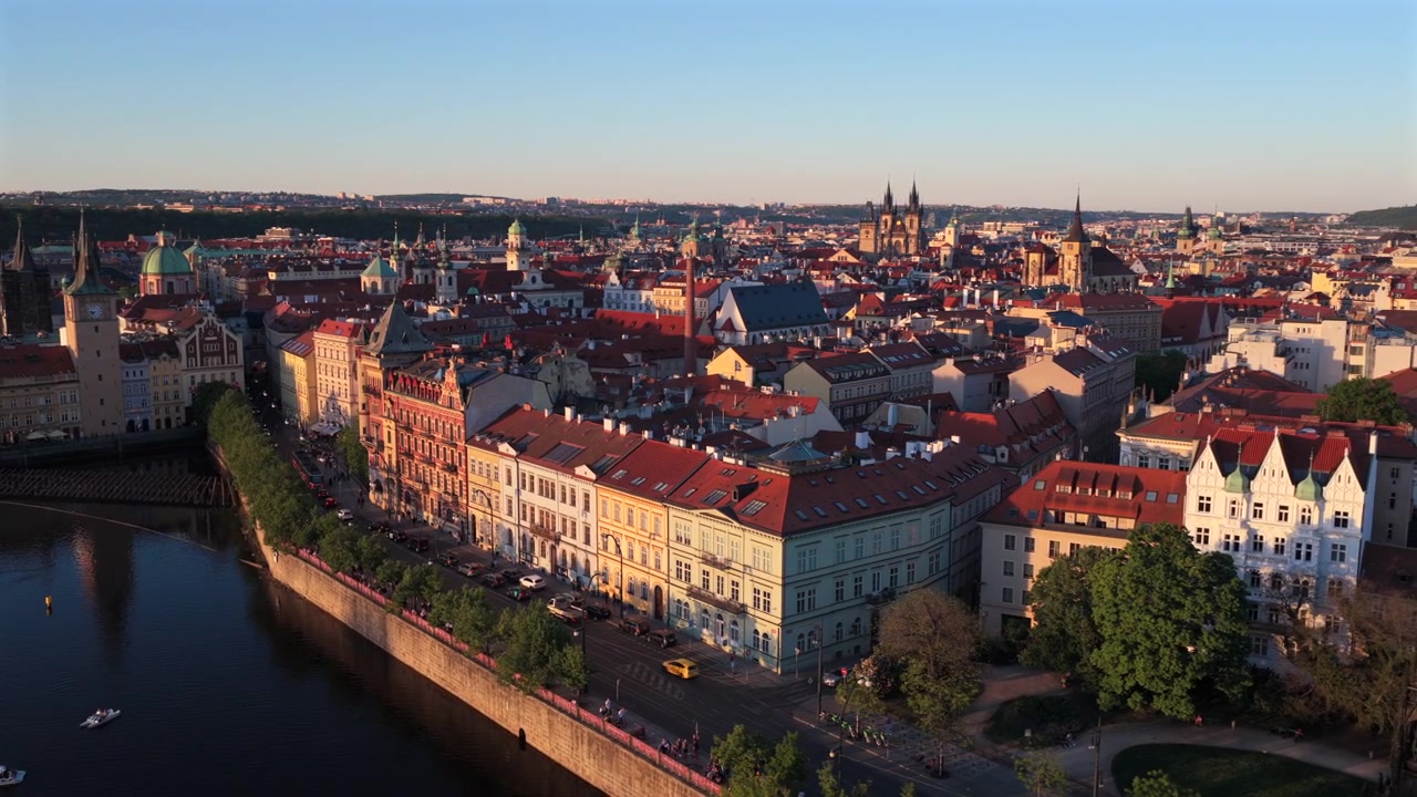Vista aerea con drone del centro storico di Praga con le guglie della Chiesa di Týn visibili sopra un mare di tetti rossi lungo la riva del fiume Moldava sotto un cielo azzurro limpido al tramonto, Praga, Repubblica Ceca.
