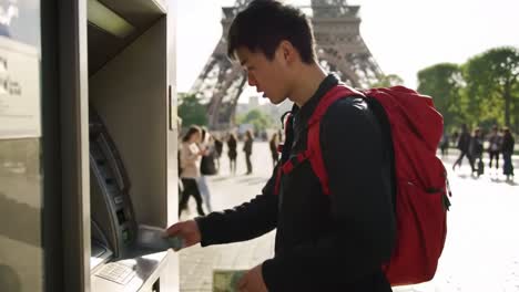young man using an atm nearby iconic landmark, engaging in daily activity amidst crowds in the city