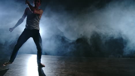 modern ballet a man from a sitting position on the stage jumps backflip with rotation on a dark stage in the smoke in the spotlight.