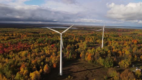 couple of wind turbines surrounded by vibrant autumn forest, aerial orbit view