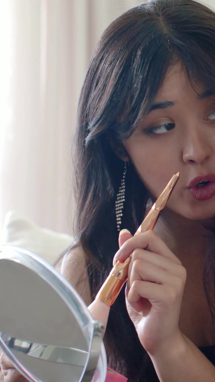 Vertical video: Holding mirror woman in tank touching up blush with gold brush on sofa, copy space