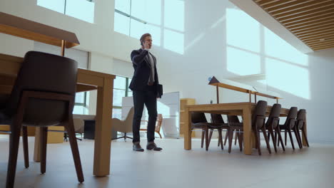 one caucasian businessman talking on phone in spacy modern meeting room with panoramic windows - push in low wide angle