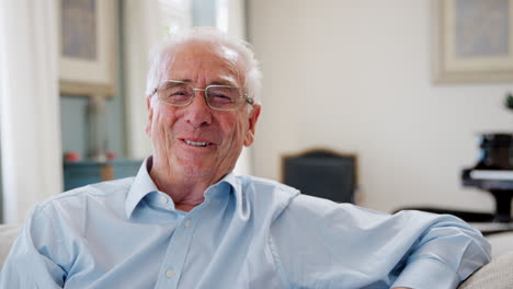 Portrait-Of-Smiling-Senior-Man-Sitting-On-Sofa-At-Home