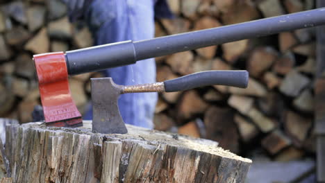 man walks behind hatchets on a stump to set logs on a stack