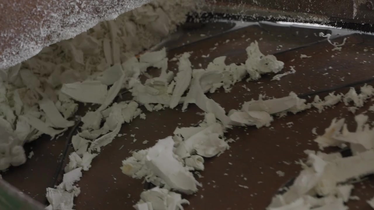 Scaglie di plastica bianca che si muovono lungo un nastro trasportatore dalla trituratrice per la rilavorazione in pellet