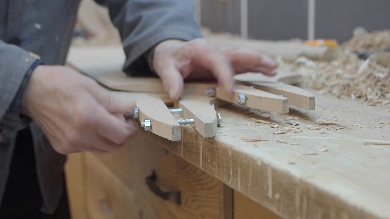 Craftsman's Hands Assembling Wooden Tool with Bolts in Workshop