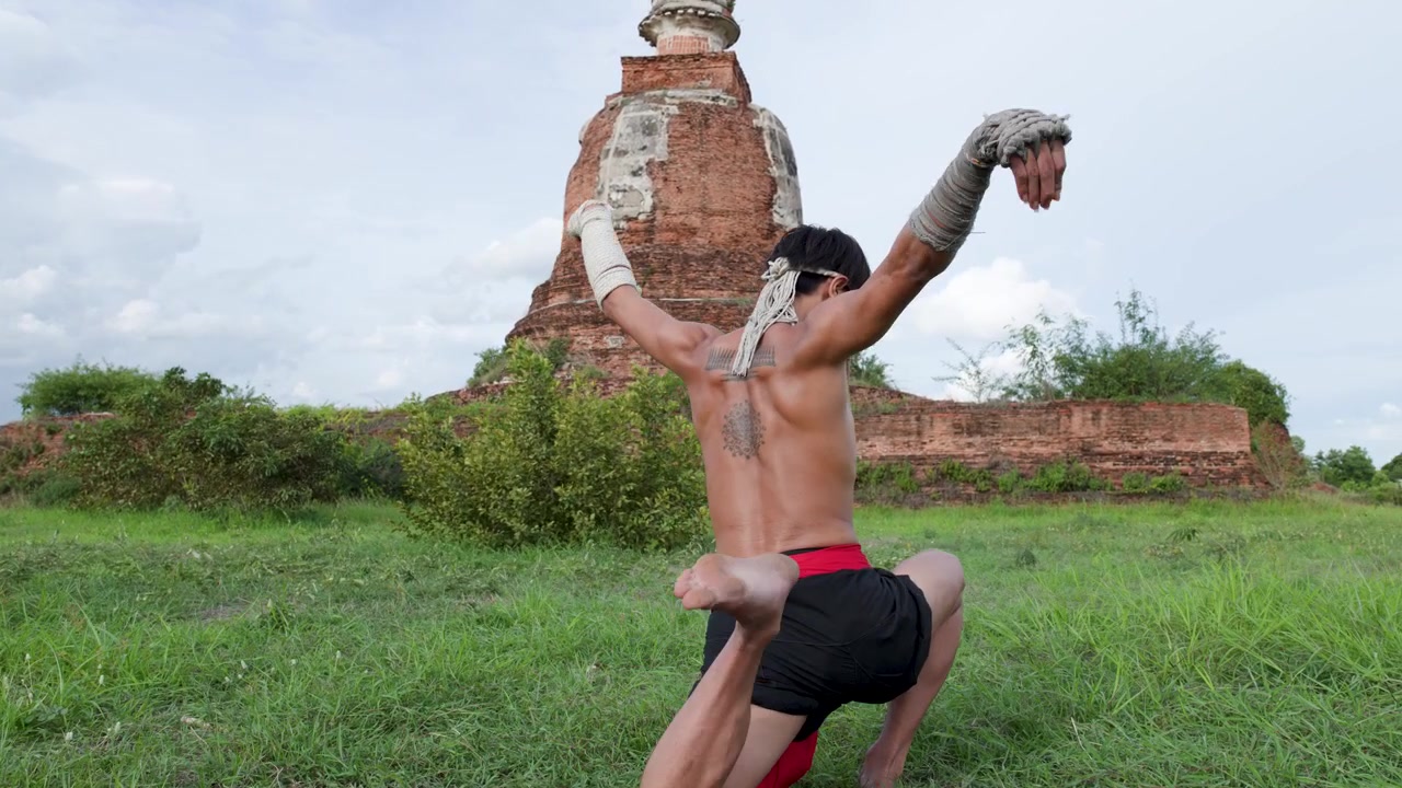 Tayland'ın Ayutthaya kentinde, antik bir pagodanın önünde geleneksel hareketler sergileyen üstsüz bir dövüşçü.